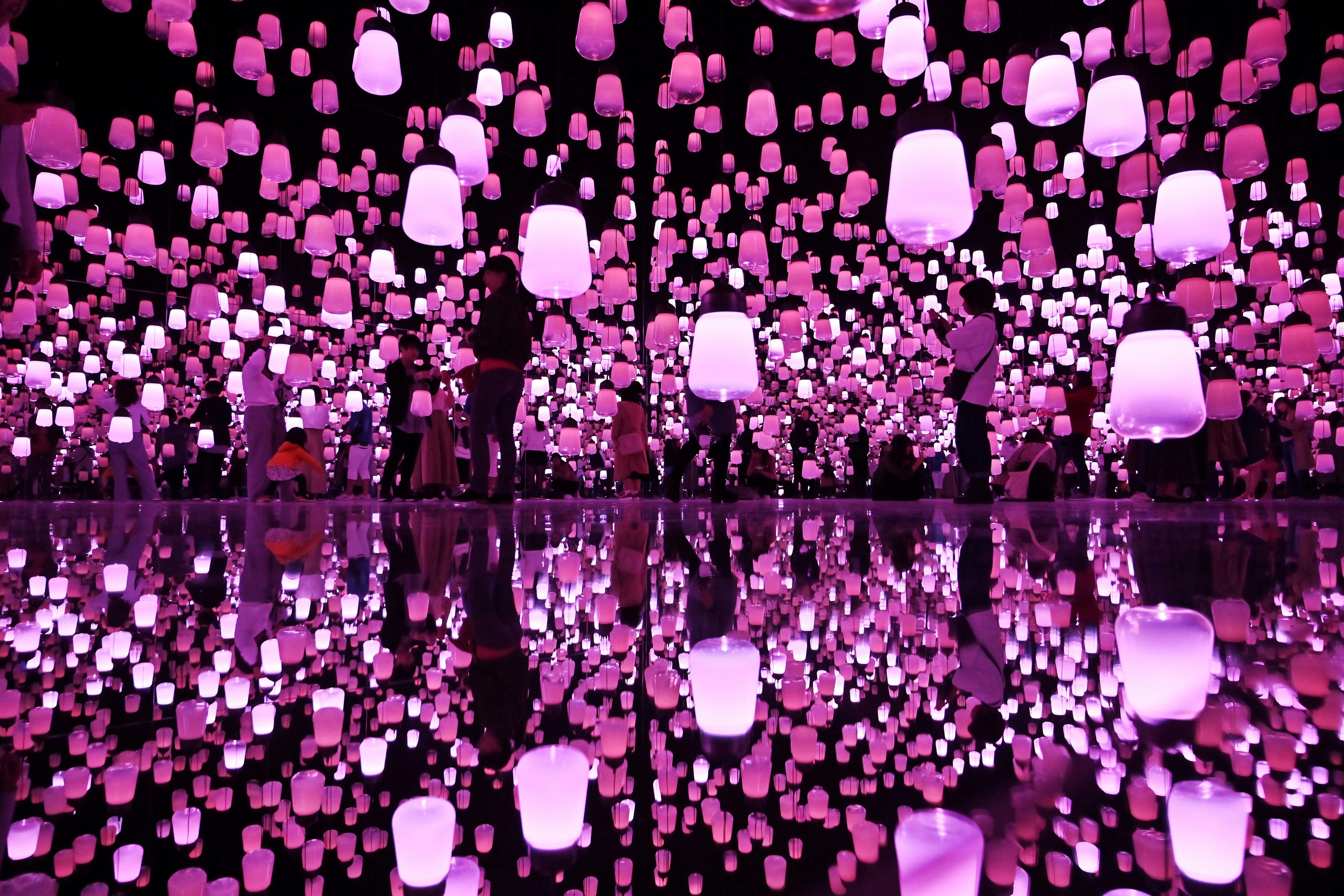 Gallery-goers are visible in silhouette in a large room which is strung with neon-pink lamps, which are reflected prettily in the mirrored floor
